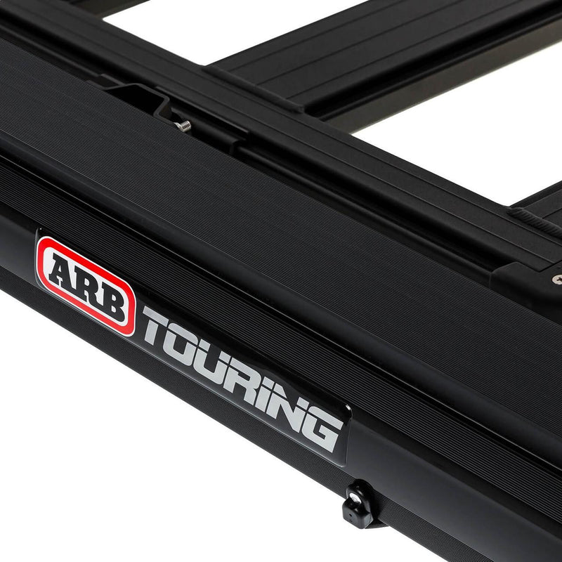 ARB Hard Case Awning 814412A mounted along the side of a black roof platform, showing the ARB Touring badge and rack mounting bracket