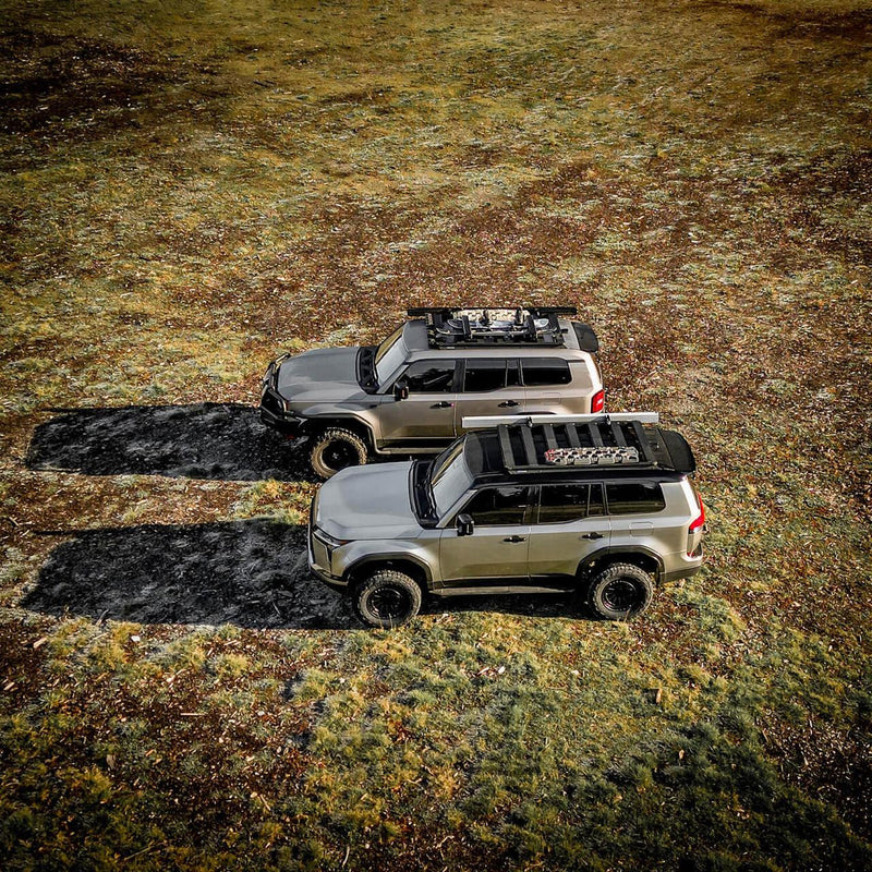 Overhead view of two four wheel drives on a grassy track, each carrying an ARB BASE Rack loaded with recovery boards and cargo