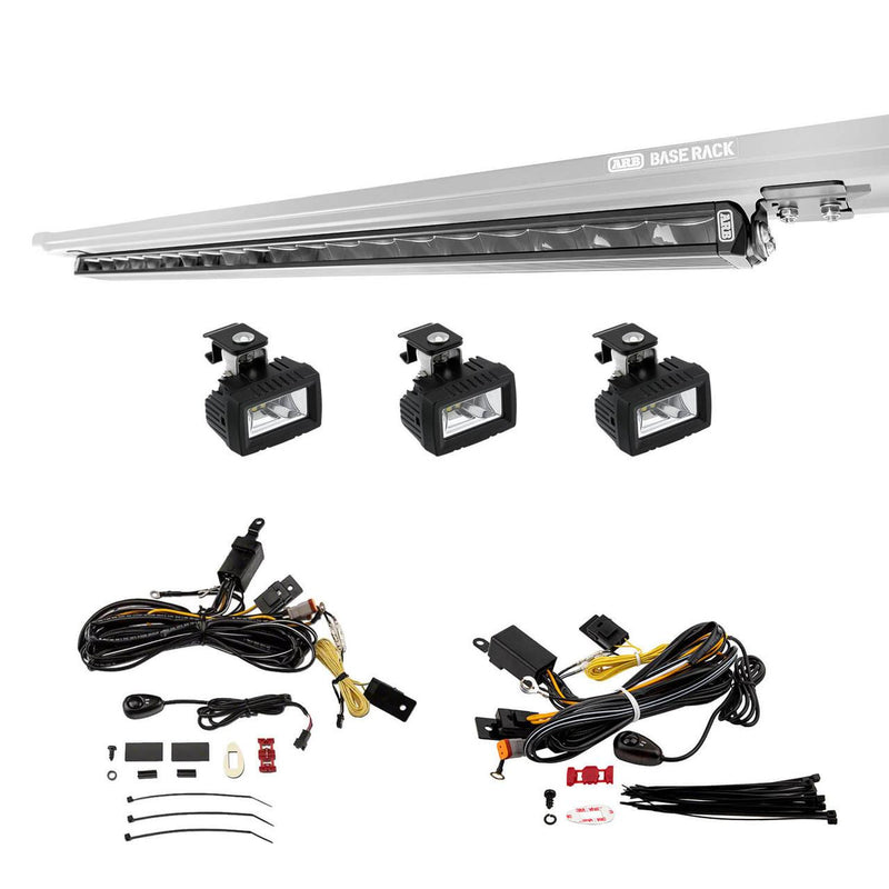 ARB BASE Rack Lighting Kit on white: the slim black light bar mounted under a BASE Rack edge, three small square auxiliary lights on dovetail brackets, and two wiring looms with switches, relays and cable ties