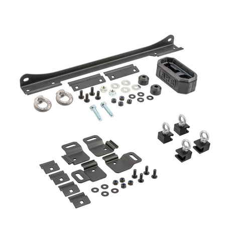 ARB BASE Rack Recovery Kit laid out on white: a long steel jack holder bracket with forged eye nuts and a rubber ARB handle keeper, four recovery board brackets with clamp plates, four eye bolt tie down blocks and the mounting hardware