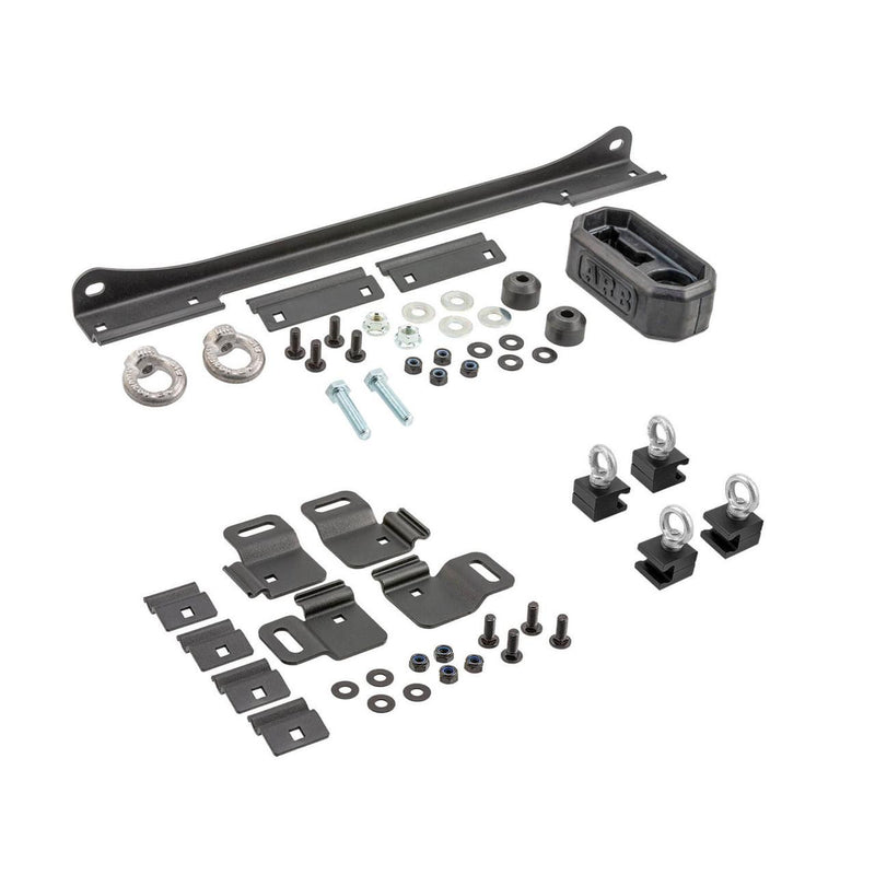 ARB BASE Rack Recovery Kit laid out on white: a long steel jack holder bracket with forged eye nuts and a rubber ARB handle keeper, four recovery board brackets with clamp plates, four eye bolt tie down blocks and the mounting hardware