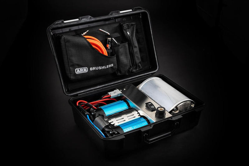 ARB CKBLTP12 brushless twin motor portable 12V air compressor shown in its open black hard case with two blue anodized BRUSHLESS motor barrels and a polished air tank, coiled leads and an orange air hose in the ARB BRUSHLESS lid pocket