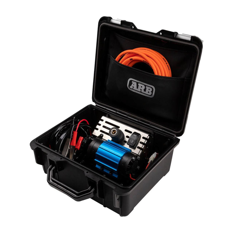 ARB CKMP12V2 portable single motor 12V air compressor in its open black hard case, with one blue anodized motor unit on a stainless panel, an ARB rocker switch and outlet fitting, coiled battery leads with red and black clamps, and an orange air hose in the ARB branded lid pocket