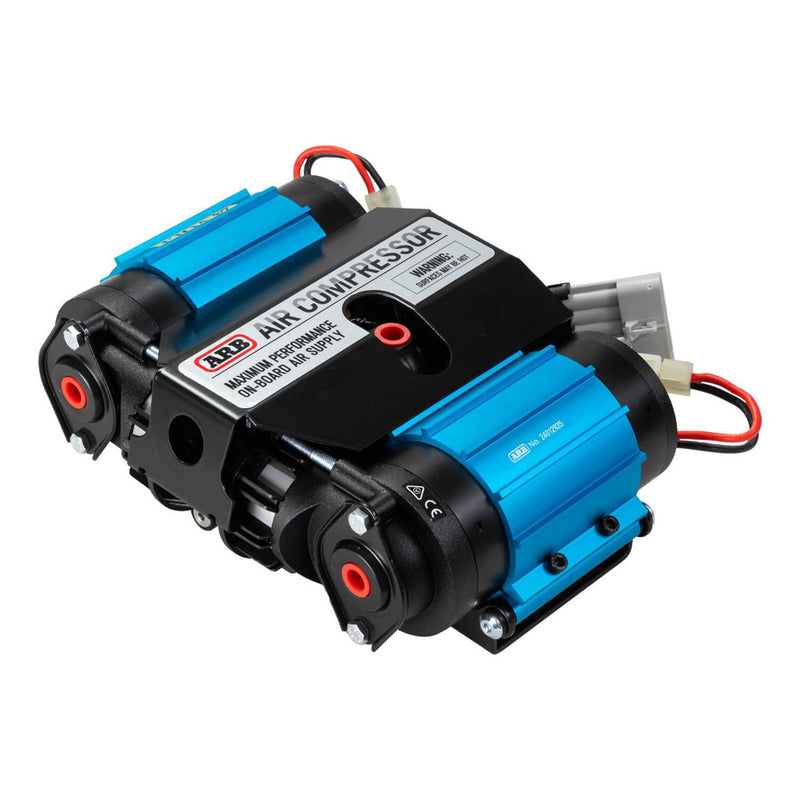 ARB CKMTA24 twin motor on-board 24V air compressor, two blue anodized motor barrels flanking a black manifold cover printed ARB AIR COMPRESSOR MAXIMUM PERFORMANCE ON-BOARD AIR SUPPLY, with two black cylinder heads, red inlet grommets and a wiring harness