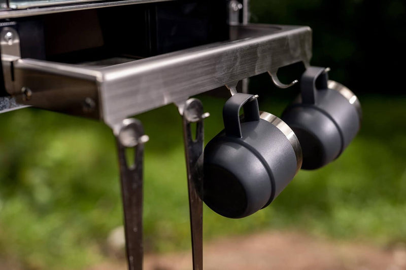 Detail of the ARB Slide Out Camp Kitchen RDKNA1045 stainless bench edge hooks with two camp mugs hung and folding support legs below