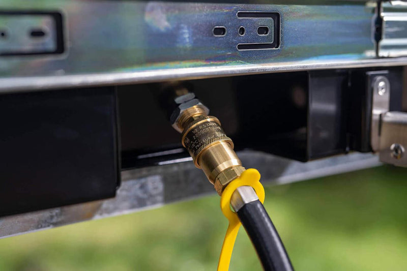 Detail of the ARB Slide Out Camp Kitchen RDKNA1045 brass gas quick-connect fitting and hose beneath the stainless frame
