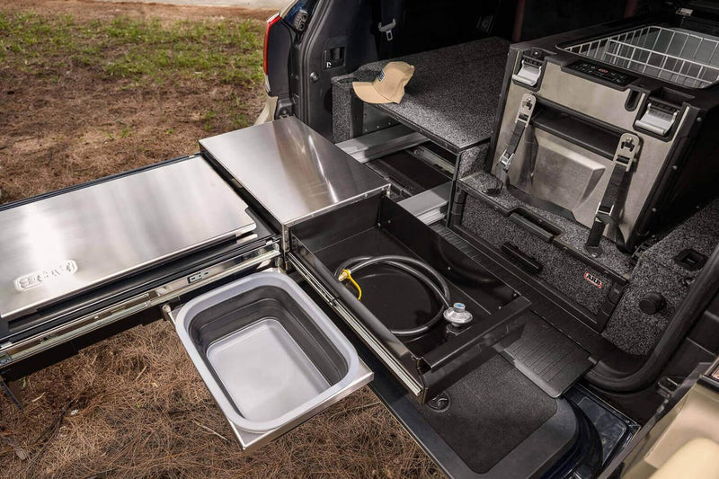 ARB Slide Out Camp Kitchen RDKNA1045 fully opened showing the collapsible sink tub, gas hose drawer and stainless bench beside an ARB fridge