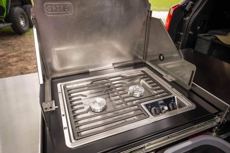 Close view of the ARB Slide Out Camp Kitchen RDKNA1045 stainless two-burner cooktop, cast trivet and ARB-branded control knobs