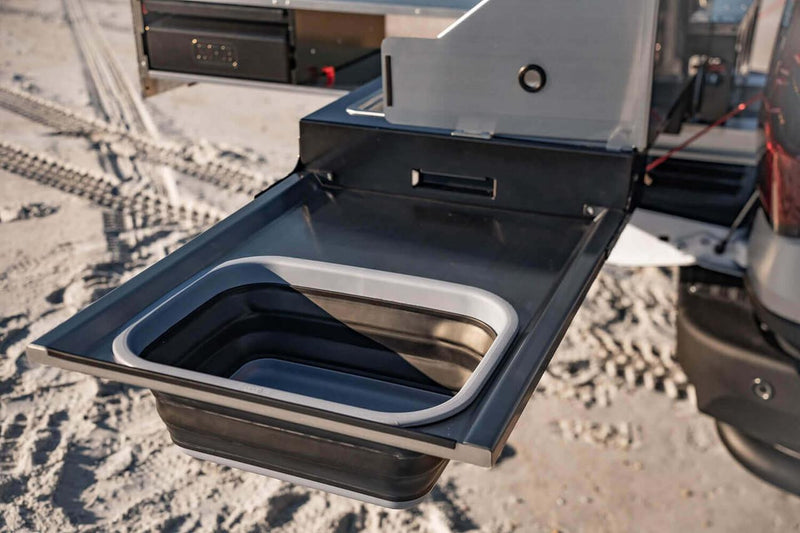 Detail of the collapsible silicone sink seated in the fold-down table of the ARB Slide Out Camp Kitchen RDKNA1355, with the stove module behind
