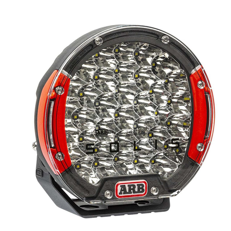 ARB Intensity Solis 36 spot driving light at an angle, large squat black die-cast body with red side accents and a clear lens over a dense reflector array, ARB INTENSITY SOLIS branding on the lens