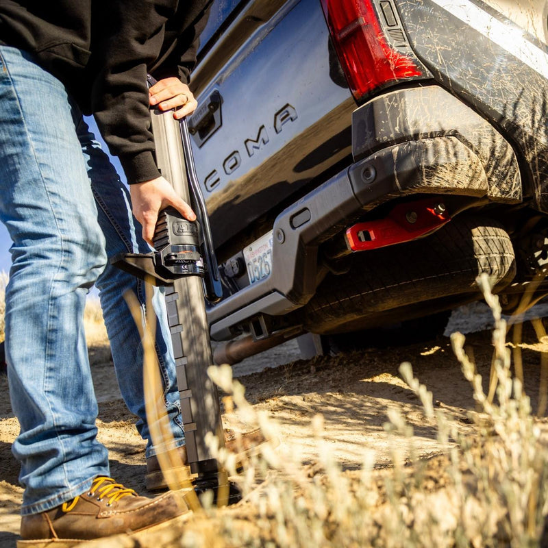Man setting the ARB JACK under a pickup's rear recovery point on a dirt track
