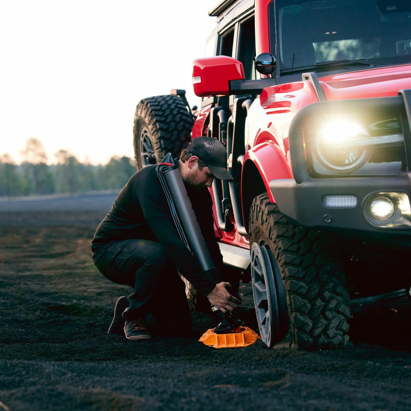 Man crouched by an SUV wheel using the ARB JACK on an orange jack base