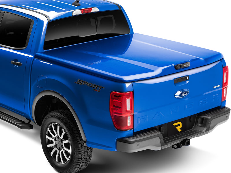 UnderCover Elite LX one-piece tonneau cover closed and latched on a pickup bed, rear three-quarter studio view, the lid sitting flush across the tailgate with no bed floor showing.