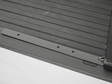 BackRack Low Profile: black low profile mounting rail lying along a white truck bed rail next to a ribbed bed liner