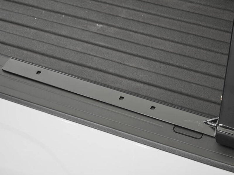 BackRack Low Profile: black low profile mounting rail lying along a white truck bed rail next to a ribbed bed liner