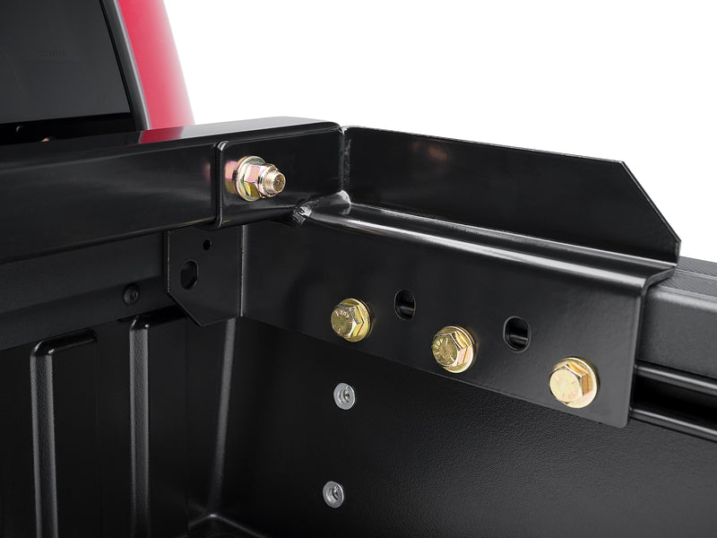 BackRack Original: close-up of a black headache rack corner bracket bolted to the front of a pickup bed with gold hardware
