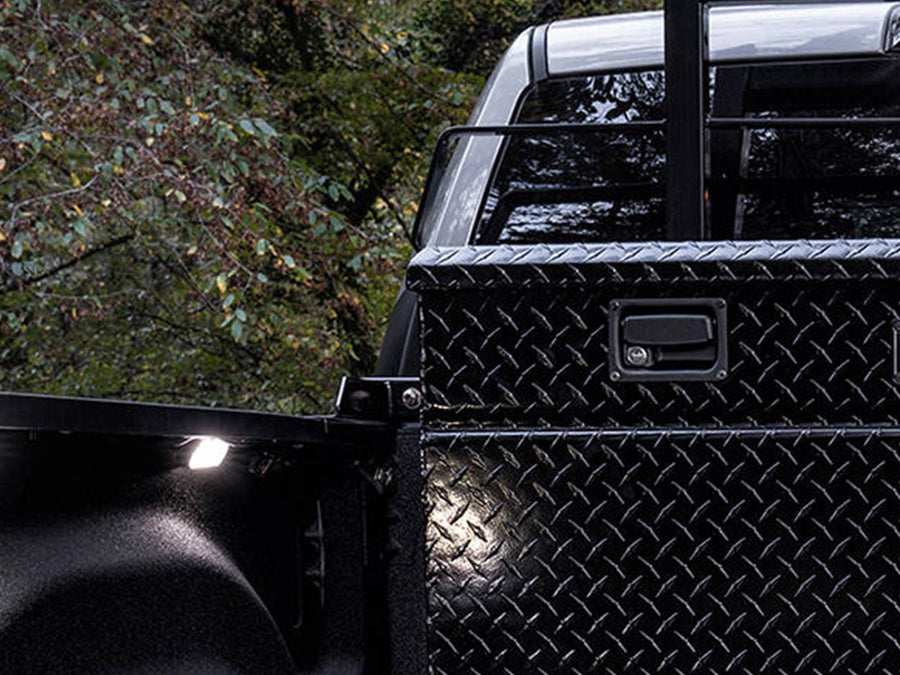 BackRack Crossover Toolbox Installation Kit: Black rack rising behind a black diamond plate toolbox on a pickup, with trees in the background.