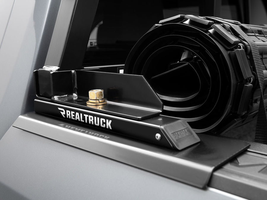 BackRack Tonneau Cover Adapter Kit: Black tonneau adapter bracket with RealTruck lettering on a gray bed rail next to a rolled-up tonneau cover.