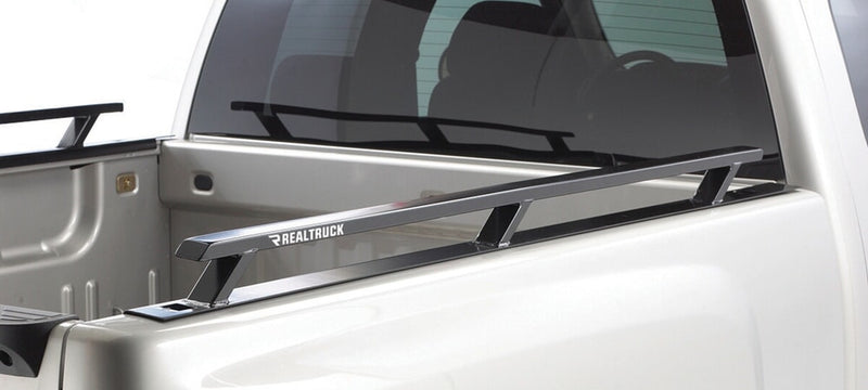 BackRack Side Rails: A black bed side rail with three stake-pocket legs runs along the top of a white pickup bed, with the matching rail visible on the far side