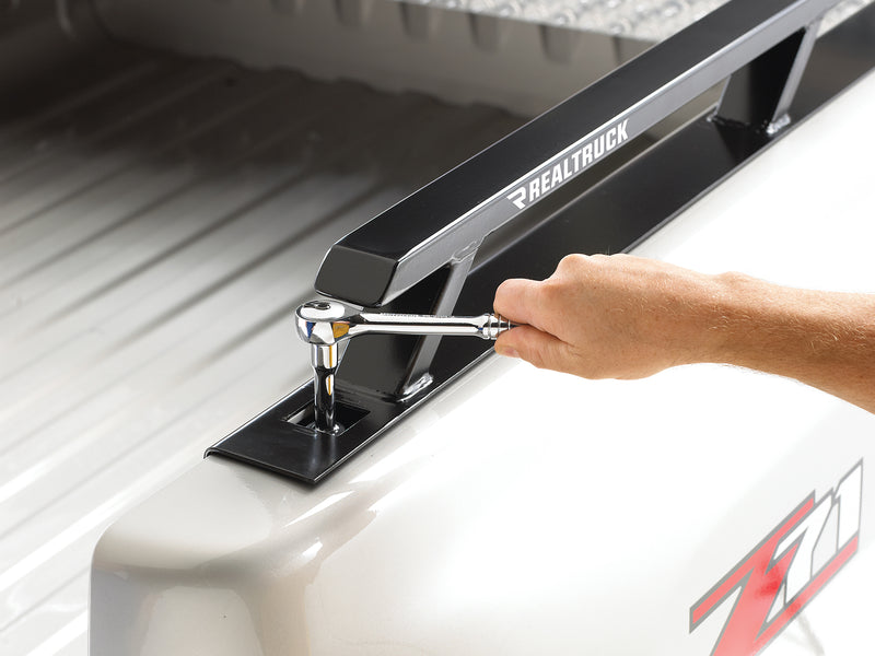 BackRack Side Rails: A hand uses a ratchet to bolt a black bed side rail stake pocket mount on a white pickup