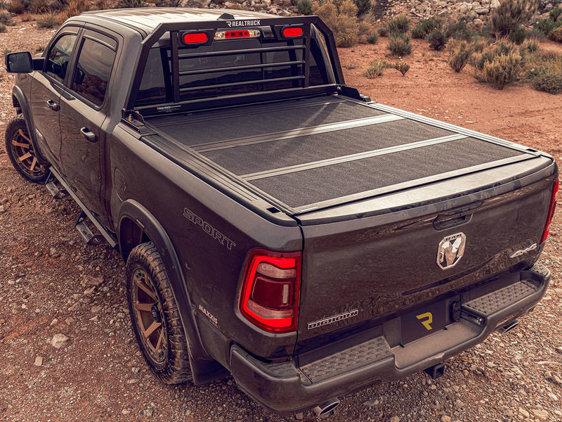 BackRack SRL: A dark Ram 1500 Big Horn with a black SRL headache rack and red lights behind a hard folding tonneau cover on desert ground
