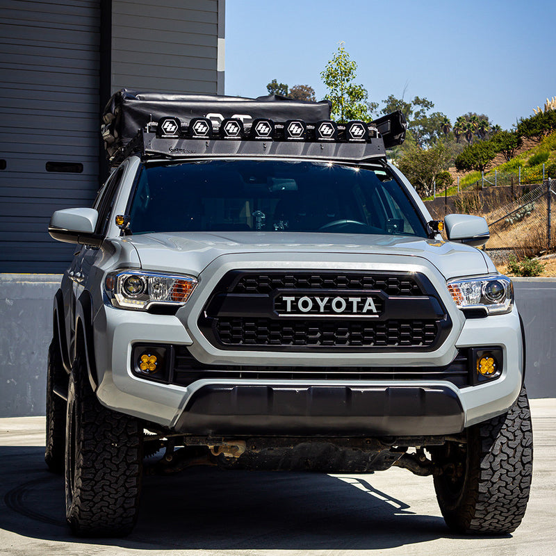 Baja Designs 7XL Linkable Roof Light Bar Kit For Prinsu Rack installed on a Toyota Tacoma: silver Toyota Tacoma with a row of linked XL pods on its roof rack and amber pods in the fog pockets