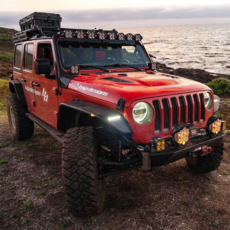Baja Designs 8XL Linkable Roof Mount Light Kit installed on a Jeep Wrangler JL: A red four-door Jeep Wrangler with Baja Designs graphics and an eight-pod roof bar sits on a coastal bluff at dusk