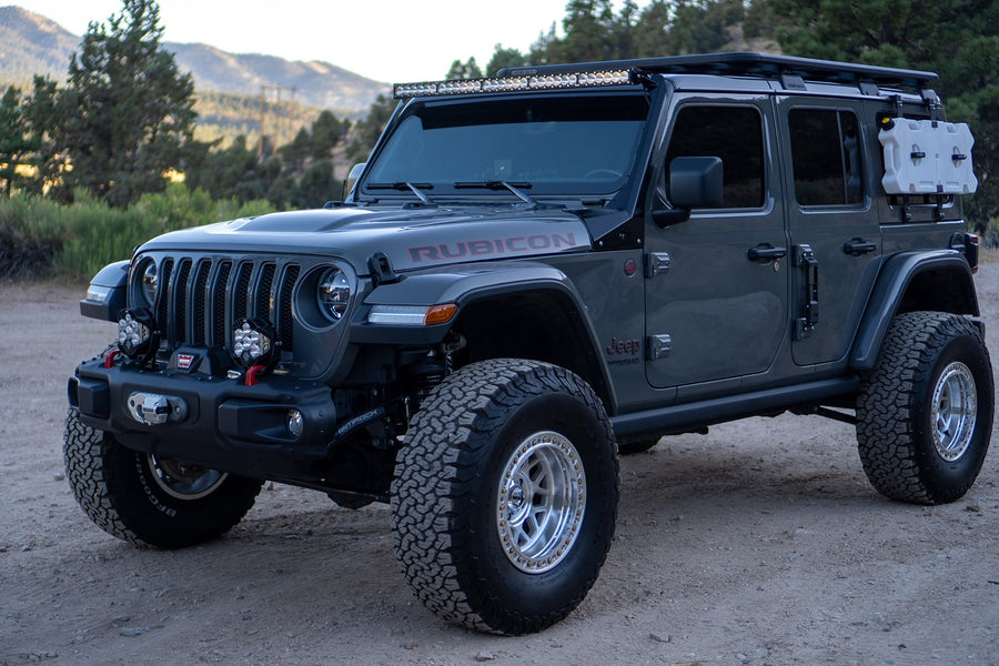 Baja Designs LP4 Pro Bumper Light Kit installed on a Jeep Wrangler Rubicon JL: A gray four-door Jeep Wrangler Rubicon with a steel bumper and roof-mounted light bar parked on a dirt lot