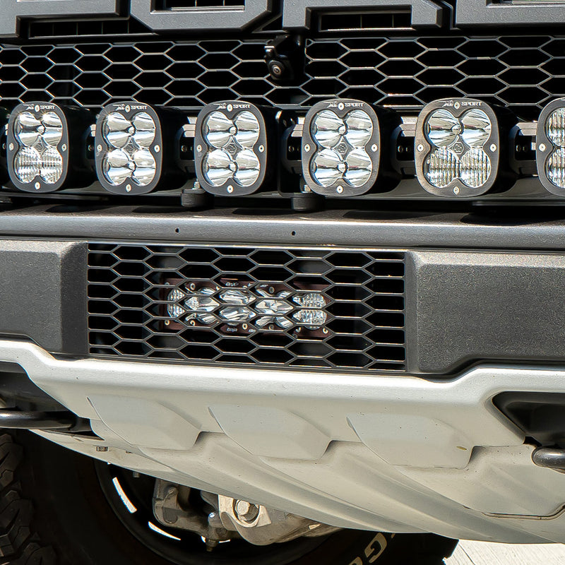 Baja Designs OnX6+ 10" Grille Lower Light Bar Kit on a Ford F-150 Raptor: close view of a truck front bumper with a lit short light bar in the lower grille below a row of square pods