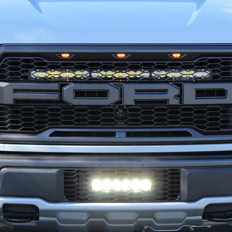 Baja Designs OnX6+ 10" Grille Lower Light Bar Kit on a Ford F-150 Raptor: front view of a Ford Raptor with a lit short light bar in the lower grille opening below the FORD grille lettering
