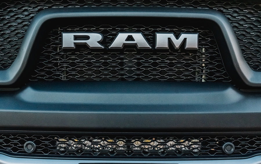 Baja Designs OnX6+ 20" Bumper Light Bar Kit on a Ram 1500: A light bar mounted in the lower grille opening of a gray Ram below the grille lettering