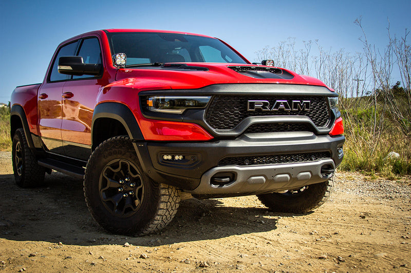 Baja Designs OnX6+ 20" Bumper Light Bar Kit installed on a Ram 1500 TRX: A red Ram 1500 TRX parked on dirt in sunlight, front three-quarter view