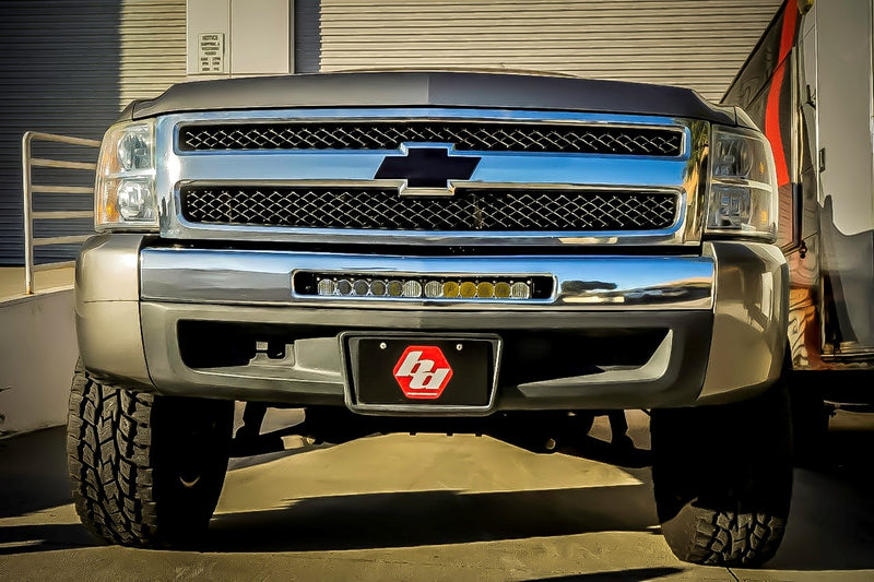 Baja Designs OnX6+ 20" Bumper Light Bar Kit installed on a Chevrolet Silverado: front view of a silver Chevrolet Silverado with a light bar mounted in the lower bumper opening and a Baja logo front plate