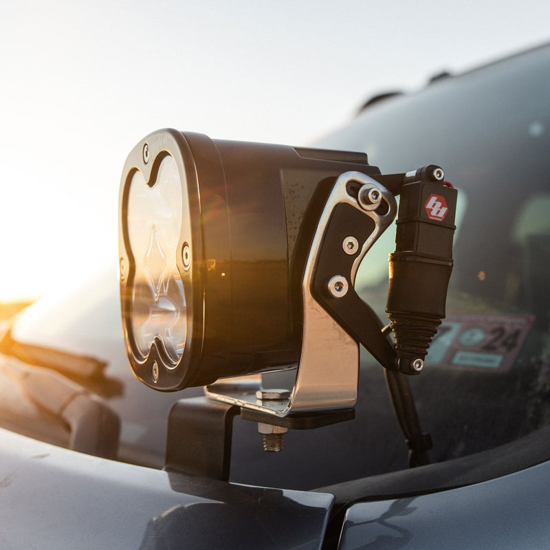 Baja Designs REFLEX Light Actuator Kit, XL Standard Housing on a vehicle: an XL pod with the REFLEX actuator on a hood-mount bracket in front of a windshield at sunset