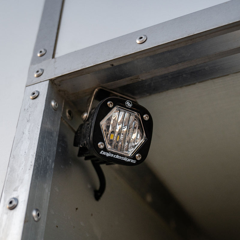 Baja Designs S1 Black LED Auxiliary Light Pod on a vehicle: A black S1 light pod with a clear lens bolted beneath an aluminum frame corner