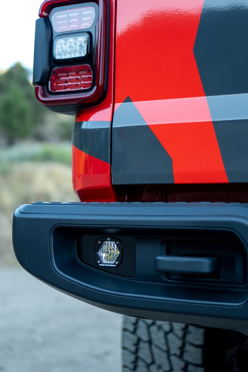 Baja Designs S1 Dual Reverse Light Kit on a Jeep Gladiator: S1 LED pod fitted in the rear bumper below the taillight of a red and gray camo Jeep Gladiator