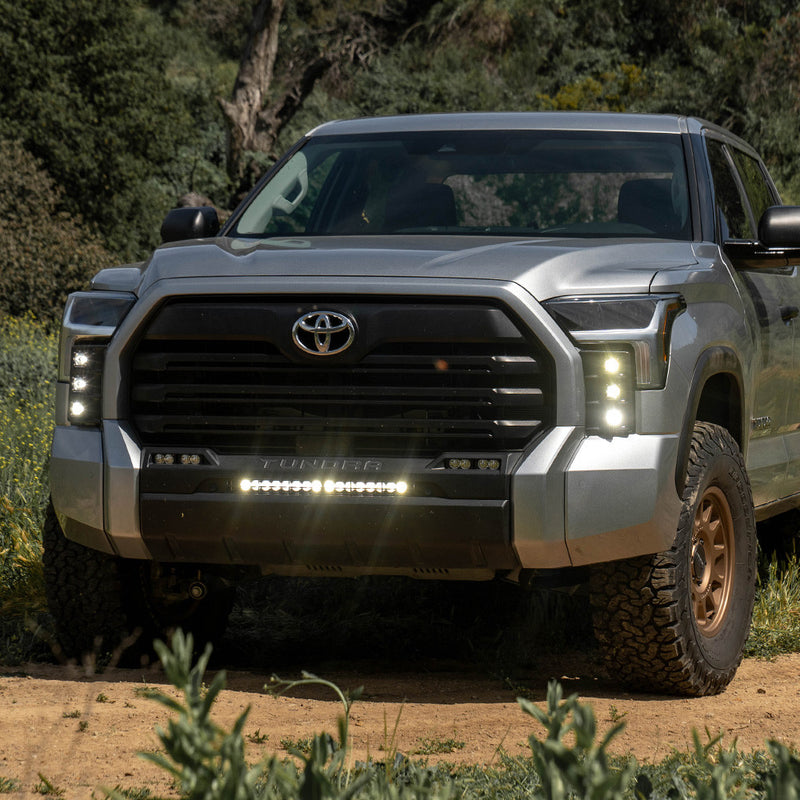 Baja Designs S1 Vent Kit installed on a Toyota Tundra: A silver Toyota Tundra parked on a dirt trail with small LED pods lit in both front bumper vents