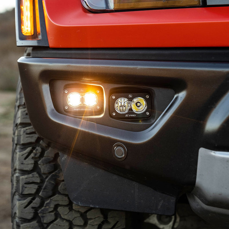 Baja Designs S2 SAE/S2 Pro Fog Pocket Kit on a Ford Raptor: close view of an S2 pod pair installed in a red Ford Raptor fog pocket, one pod lit beside the bumper