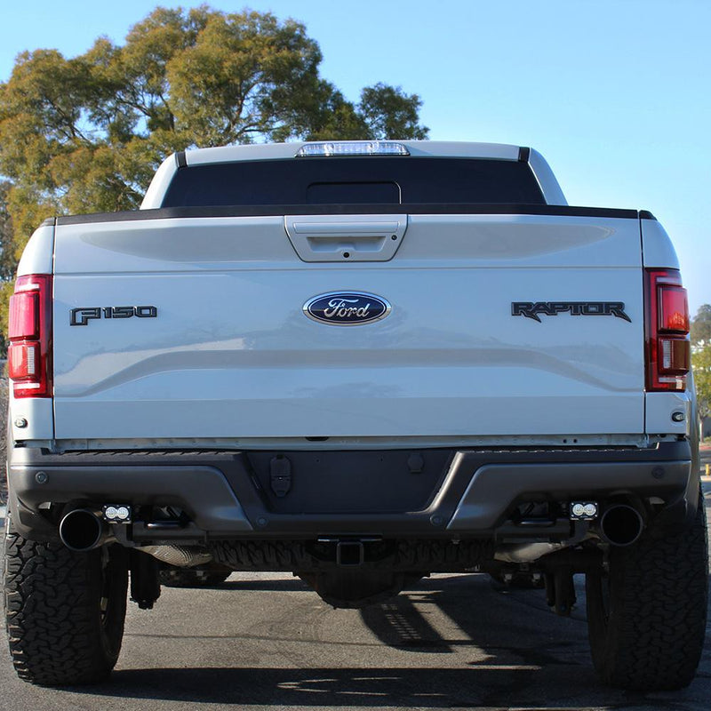 Baja Designs S2 Sport Dual Reverse Light Kit installed on a Ford F-150 Raptor: rear view of a white Ford F-150 Raptor with two reverse light pods mounted under the bumper