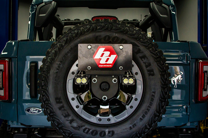 Baja Designs S2 Sport Dual Reverse Light Kit on a Ford Bronco: two S2 pods mounted in the spare tire center of a blue Ford Bronco under a Baja Designs logo plate