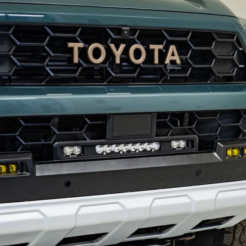 Baja Designs S8 10"/S2 Pro Grille Light Replacement Kit on a Toyota: front view of a teal Toyota grille with an S8 light bar and two S2 Pro pods mounted below the TOYOTA lettering