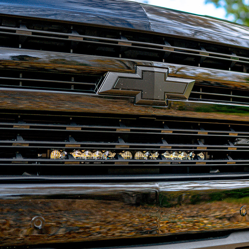 Baja Designs S8 20" Grille Light Bar Kit on a Chevrolet Silverado 1500: close view of a black Chevrolet grille with a lit light bar set behind the grille slats below the bowtie