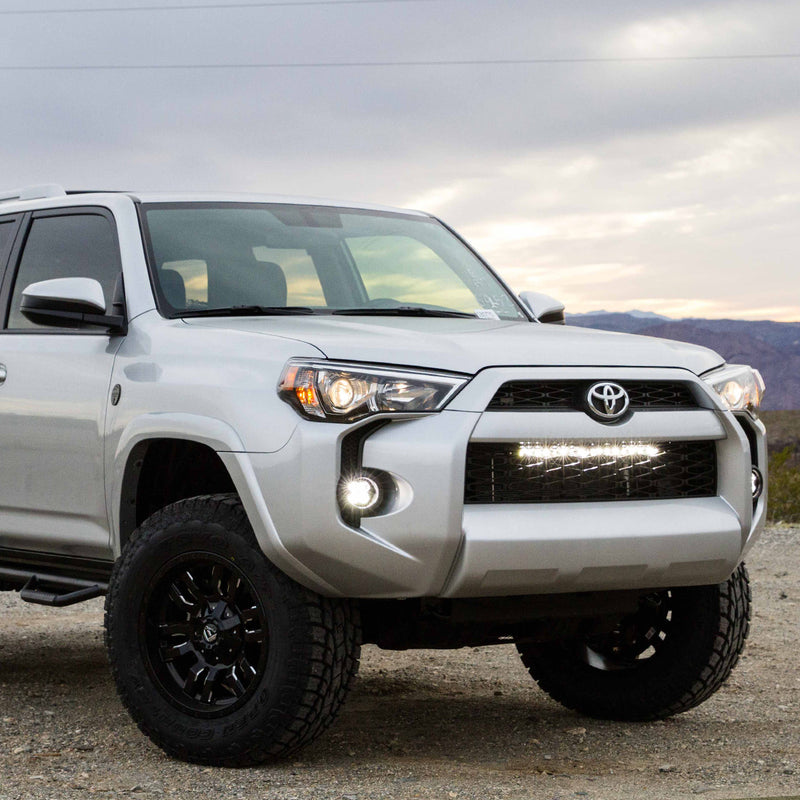 Baja Designs S8 30" Grille Lower Light Kit installed on a Toyota 4Runner: A silver Toyota 4Runner on a gravel overlook with a lit light bar across the lower grille