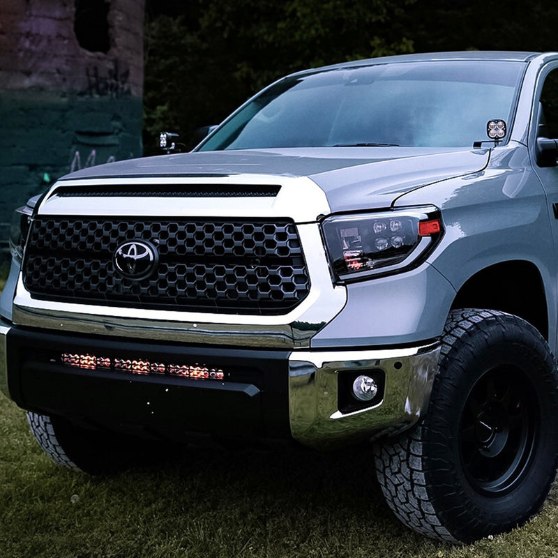 Baja Designs S8 30" Grille Lower Light Kit installed on a Toyota Tundra: A silver Toyota Tundra on grass with a lit S8 light bar glowing in the lower grille opening