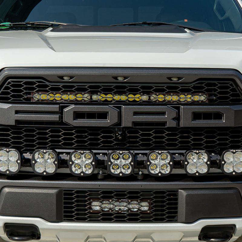 Baja Designs S8 30" Grille Upper Light Bar Kit on a Ford F-150 Raptor: front view of a white Ford Raptor with a light bar across the upper grille and a row of square pods on the bumper