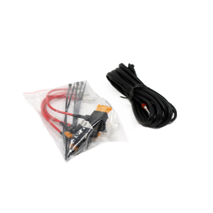 Baja Designs S8 Series Backlight Add-on Wiring Harness, whole product on a studio background: coiled black backlight harness beside a clear bag of red leads and orange connectors on white