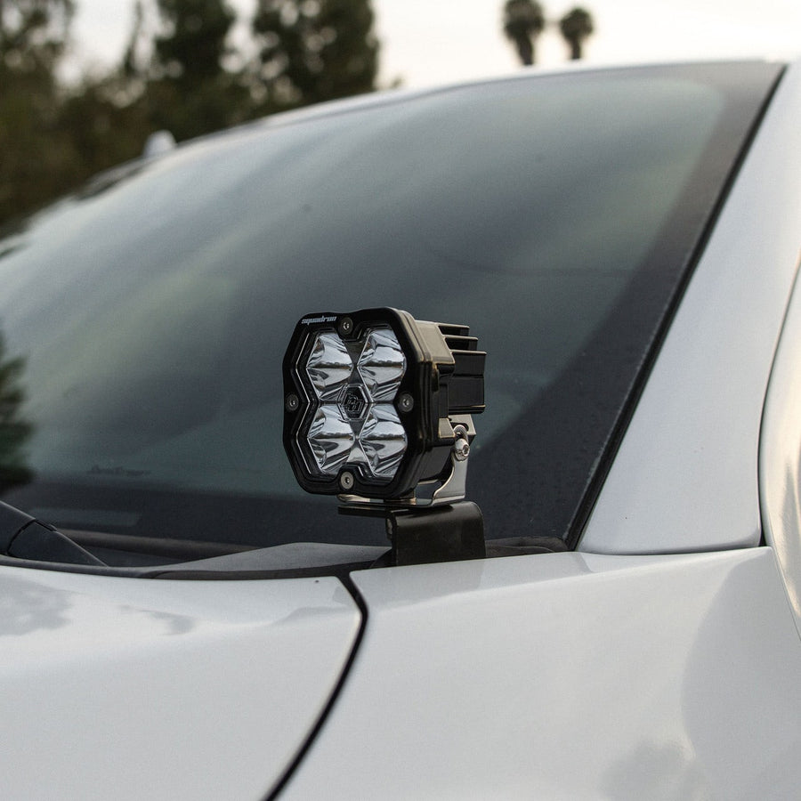 A-Pillar Light Kits by Baja Designs: A Squadron pod on an A-pillar bracket at the windshield corner of a silver vehicle.