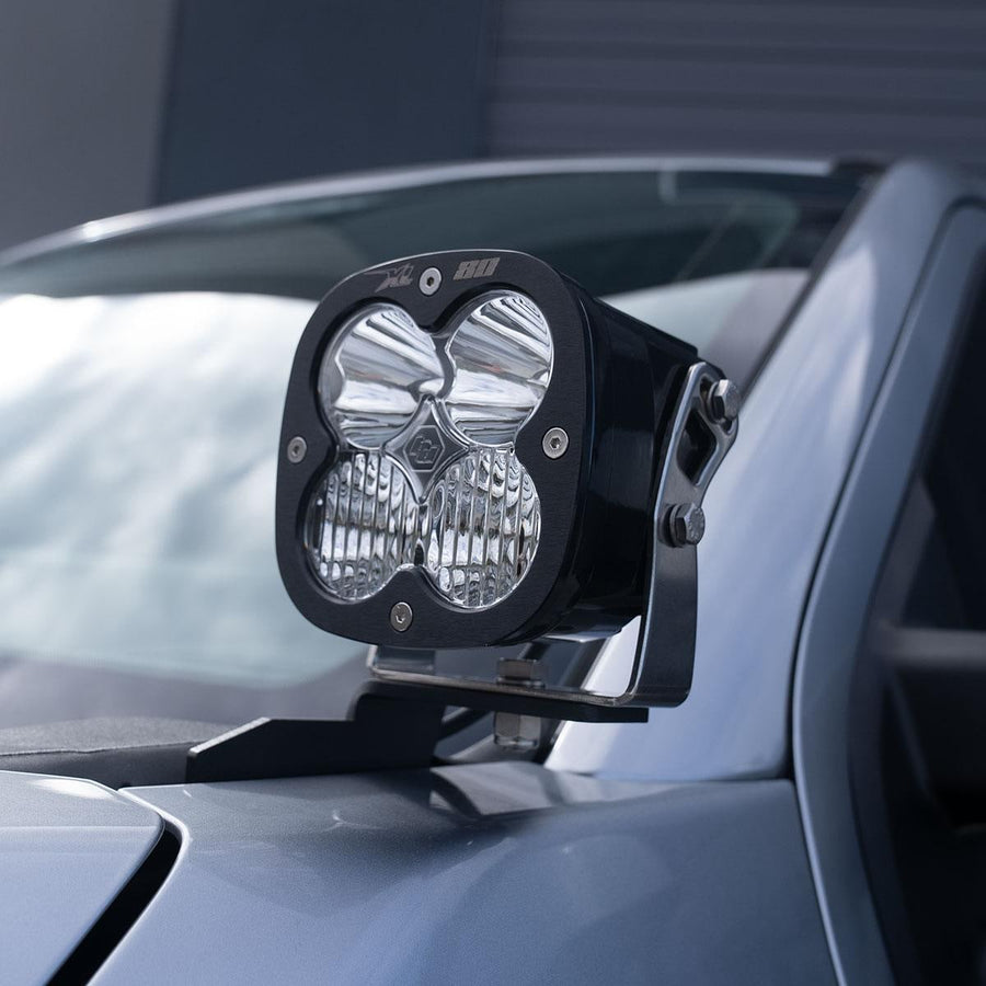 A-Pillar Light Kits by Baja Designs: A Baja Designs XL80 LED pod mounted on an A-pillar bracket beside the windshield of a gray truck.