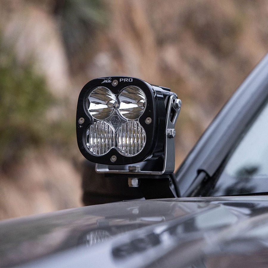 A-Pillar Light Kits by Baja Designs: An XL Pro LED pod with a clear combo lens mounted on an A-pillar bracket next to a dark truck hood.