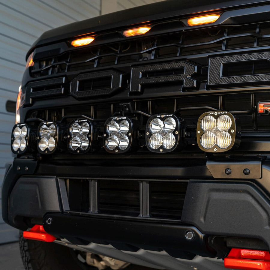 Bumper Light Kits by Baja Designs: Close front view of six XL linkable pods mounted across the grille opening of a black Ford Raptor with amber grille marker lights.